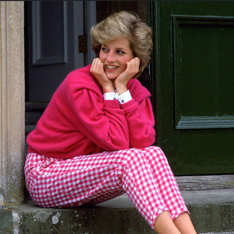 Princess Diana sitting in pink sweater, gingham plaid pants.